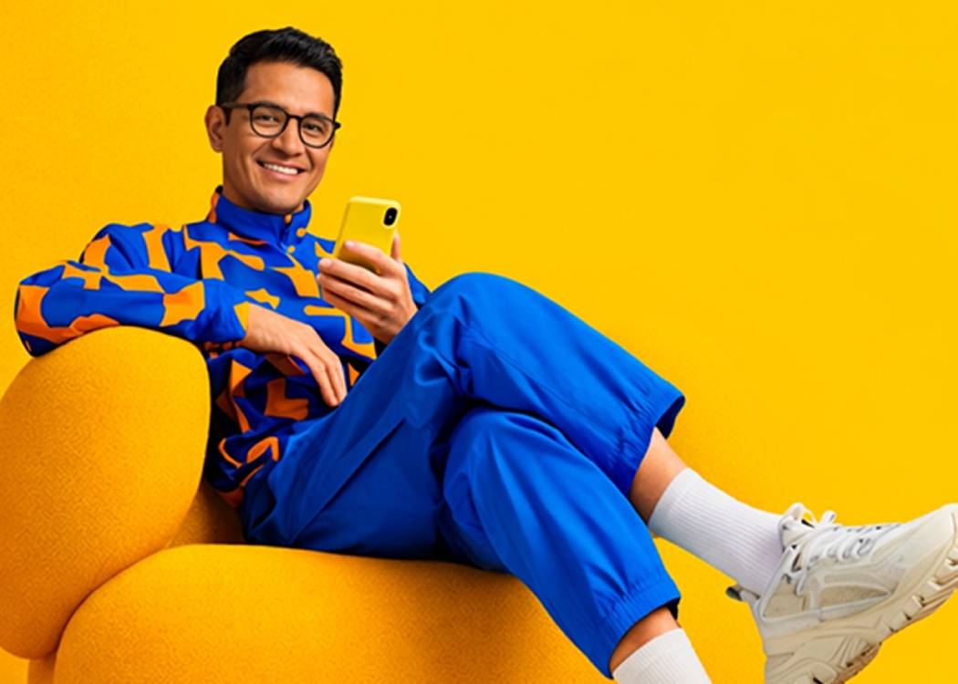 Hombre sentado en un sillón amarillo mirando su teléfono
